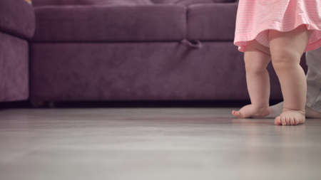 Kid feet walking on floor. Close up of baby learning to walk. Toddler going with mother support. Baby feet stepping at home. Child first step. Mother learning walk daughter. Baby care conceptの写真素材