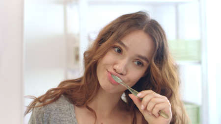 Attractive woman using toothbrush and toothpaste for brush teeth front mirror in bathroom. Portrait cheerful woman brushing teeth in morning bathroom. Morning freshness and dental careの写真素材