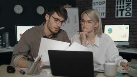 Business couple working together with document data front laptop in night office. Overworked man and...