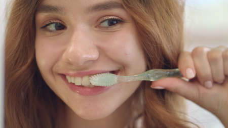 Smiling woman brushing teeth with brush in mirror at home bathroom. Close up portrait happy woman cleaning teeth with toothbrush and toothpaste in bath room. Teeth care and dental hygieneの写真素材
