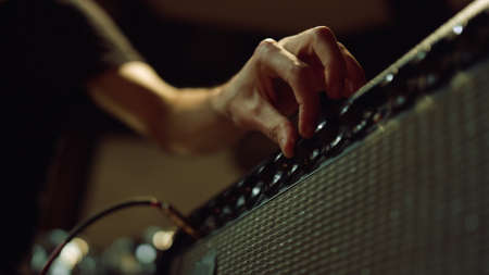 Unknown sound engineer preparing equipment for concert in dark hall. Man hand turning knobs on...