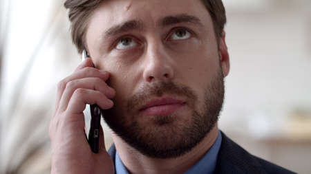 Portrait of young businessman talking phone at remote office. Focused man discussing on cellphone in...