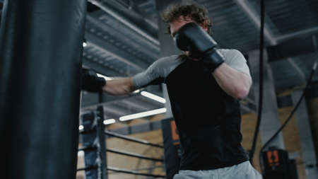 Closeup angry kickboxer hitting punching bag at gym. Wicked sportsman training kicks in sport club. Agitated fighter working on blows in fitness center.の写真素材