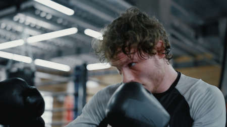 Portrait of active kickboxer training blows at gym. Closeup energetic sportsman hitting punching bag...