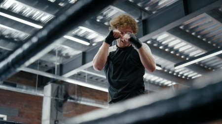 Aggressive kickboxer making punches at gym. Strict sportsman doing hits on ring. Ambitious fighter training kicks before battle in fitness center.の写真素材