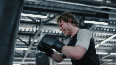 Anxious fighter hitting punching bag at gym. Closeup aggressive kickboxer working on blows in sport...