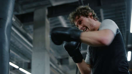Portrait of natural kickboxer boxing at gym. Closeup candid sportsman exercising in sport club. Emotional fighter hitting boxing bag in fitness center.の写真素材