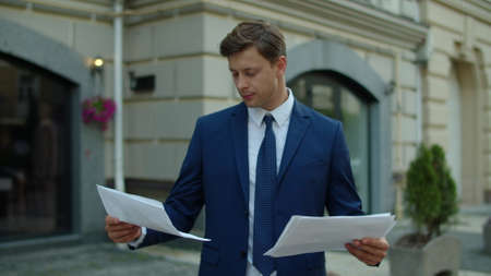 Focused businessman reading financial report outdoors. Thoughtful business man analyzing project data in papers at street. Close up of serious professional working with documents outside.の写真素材