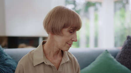 Portrait of senior woman posing at camera. Closeup positive woman sitting on sofa in living room. Older lady smiling at home. Mature woman with stylish hairstyle looking at cameraの写真素材