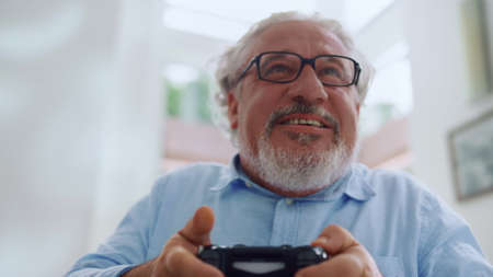 Portrait of smiling senior man playing video game. Emotional old man using gamepad for computer...