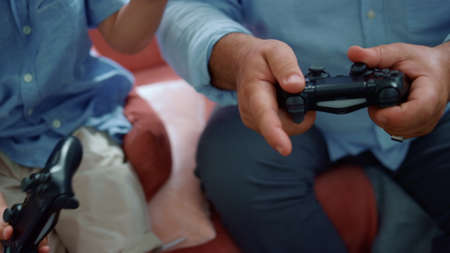 Boy and man hands playing video game with gamepads. Closeup grandparent and grandchild using game...