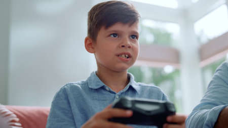 Portrait of serious boy using gamepad for computer game. Male gamer pushing buttons on joystick. Happy boy winning video game at home. Closeup excited child celebrating victory after game competitionの写真素材