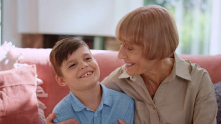 Happy grandmother hugging grandson in living room. Smiling boy talking with senior woman. Portrait...