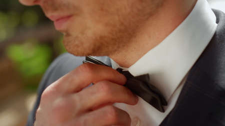 Closeup handsome man smiling in garden. Portrait of young male person touching bow tie outdoors....