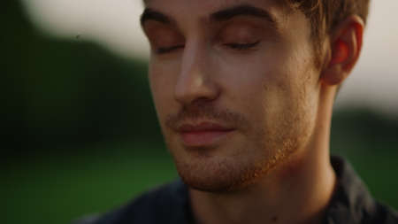 Smiling man looking at camera outdoors. Portrait of relaxed man feeling shy in summer park. Closeup handsome male person hesitating on meadow. Attractive man posing at sunset outside.の写真素材