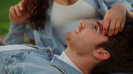 Portrait of brunette girl stroking guy hair outdoors. Closeup young man and woman lying on gree grass at summer picnic. Love couple spending time on romantic date in park.の写真素材