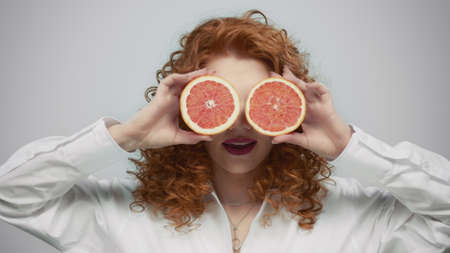 Happy woman holding grapefruit pieces in hands on grey background.の写真素材