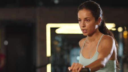 Portrait of sporty girl using velosimulator in sport club. Attractive fitness woman exercising on...