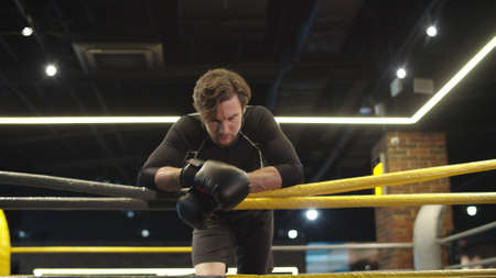 Calm fitness man looking at camera in sport club. Closeup sporty male boxer standing on boxing ring. Relaxed sport man having break after fight at gym.の写真素材