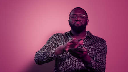 Closeup happy african man holding stack of money indoors. Portrait of smiling afro guy throwing dollars on pink background. African american man throwing cash money in studio.の写真素材