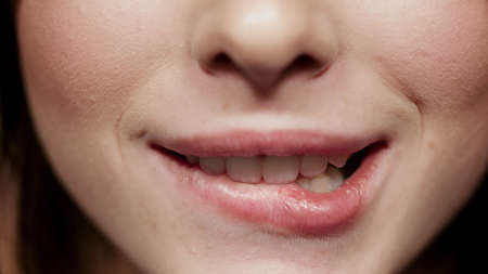 Macro of sexy lower part of female person face videotaping in studio. Closeup charming woman mouth smiling indoors. Playful girl biting lip in atelier.の写真素材