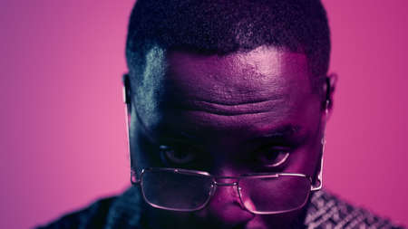 Closeup serious afro guy raising head up indoors. Portrait of focused man looking at camera on pink background. African american man staring at lens in studio.の写真素材