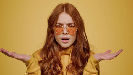 Portrait of frustrated female person looking at camera indoors. Upset girl making hand gestures on orange background. Closeup curious woman acting in studio.の写真素材
