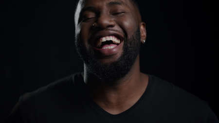 Closeup happy african male person posing on black background. Portrait of joyful afro guy laughing...