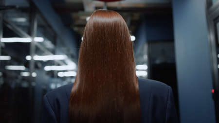 Back view serious businesswoman walking in office corridor. Closeup beautiful business woman with long hair going in business center hallway. Focused female professionalwalking in corporate interior.の写真素材