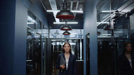 Portrait of smiling businesswoman posing in office corridor. Closeup charming female manager looking at camera in office hallway. Positive business woman holding folder in business center interior.の写真素材