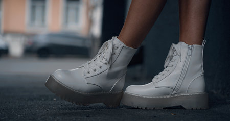 Woman legs standing in urban background near road with cars. Close up young female legs in white shoes posing in modern city street. Side view girl wearing white shoes. Urban fashion concept.の写真素材