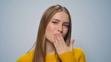 Portrait positive woman sending air kiss to camera in slow motion. Closeup happy girl flirting on grey background. Cheerful lady smiling in studio. Smiling model posing on camera. Love conceptの写真素材