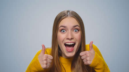 Portrait of positive woman showing thumb up at camera on grey background. Playful lady dancing in...