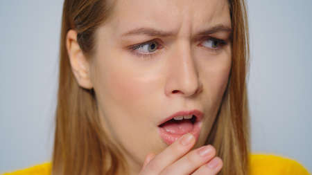 Closeup young sick woman coughing on grey background. Close up ill girl feeling bad in studio....