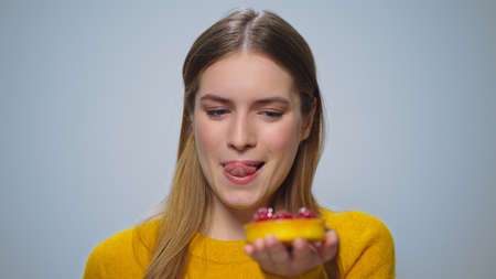 Portrait pensive woman selecting between apple or cake on grey background. Closeup happy girl showing unhealthy and healthy food at camera. Attractive lady choosing cake in studio. Food addictionの写真素材