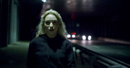 Beautiful woman going towards camera at night highway in city lights. Sexy female model walking...
