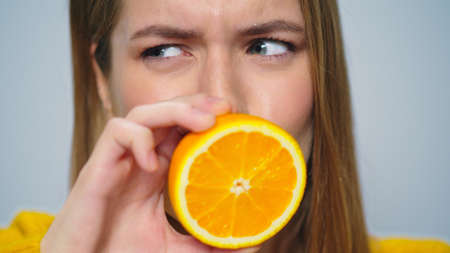 Closeup positive woman making funny faces with orange in hands in studio. Portrait happy girl smiling at camera. Joyful lady having fun on grey background. Playful model making grimaces indoors.の写真素材