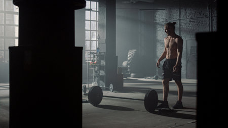 Young sportsman checking weights before lifting barbell in sports club. Male bodybuilder preparing sports equipment for strength exercises in gym. Shirtless man rubbing hands with magnesiumの写真素材
