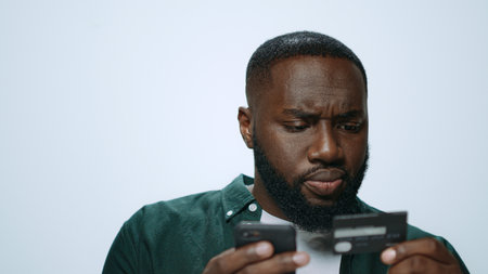 Portrait serious man shopping online smartphone in studio. Closeup bearded multiracial guy using credit card online payment on grey background. Focused african american student buy phone. Ecommerceの写真素材