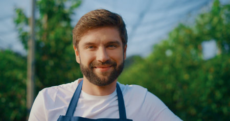 Professional plantation worker smiling camera in orchard. Happy farmer posing in work clothes at agriculture farm. Portrait of young entrepreneur looking in nature background. Organic farming concept.の写真素材