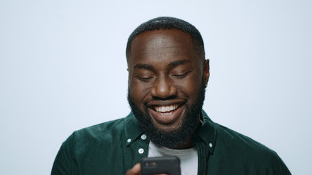 Happy african american man browsing internet online on mobile phone in studio. Portrait smiling man...