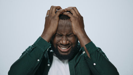 Portrait stressed man holding hands on head at grey background. Closeup african american male student having stress in studio. Tired guy having headache. Guy trouble problem fault depression conceptの写真素材