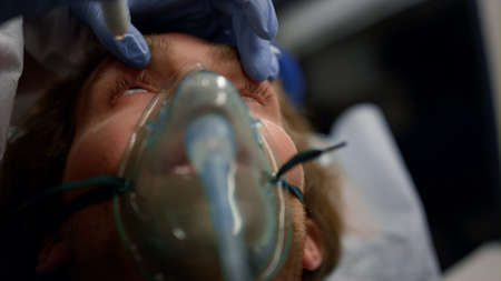 Closeup paramedic hand checking unconscious man with flashlight. Doctor in glove examining male...