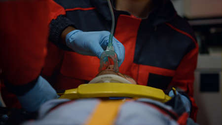 Emergency care doctors putting on non invasive ventilation mask on man. Paramedics fixing patient on stretchers with oxygen mask. Medical assistants performing first aid in ambulance carの写真素材