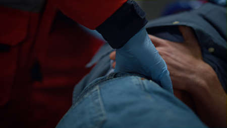 Closeup paramedic doctor hands providing first aid help of man in ambulance car. Unrecognizable medical worker in gloves checking patient kidneys. Health care professional rescuing victimの写真素材