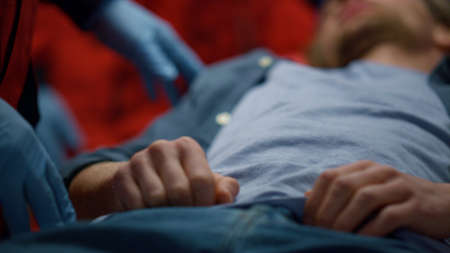 Unrecognizable doctor standing at patient. Closeup male victim lying on stretchers. Ambulance paramedic doing medical checkup of man. Medical worker wearing medical gloves. Medicine and health conceptの写真素材