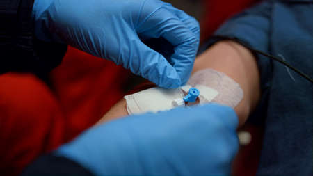 Closeup paramedic fixing medical plaster on man hand with catheter in vein. Unrecognizable doctor...