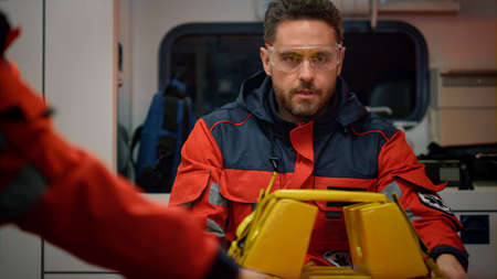 EMS paramedics preparing stretcher for emergency care. Emergency medical doctors rushing for car accident in ambulance car. Medical team wearing protective glasses and red uniform for workの写真素材