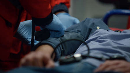 Exhausted man lying on stretchers in emergency vehicle. Paramedic ambulance hands using medical equipment for emergency care. Medical worker putting tonometer cuff on patient arm. Rescue conceptの写真素材