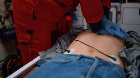 Paramedic hands performing CPR of injured man on stretchers in emergency car. Medical assistant in gloves doing cardiopulmonary resuscitation on patient chest. Male medic saving life of victimの写真素材